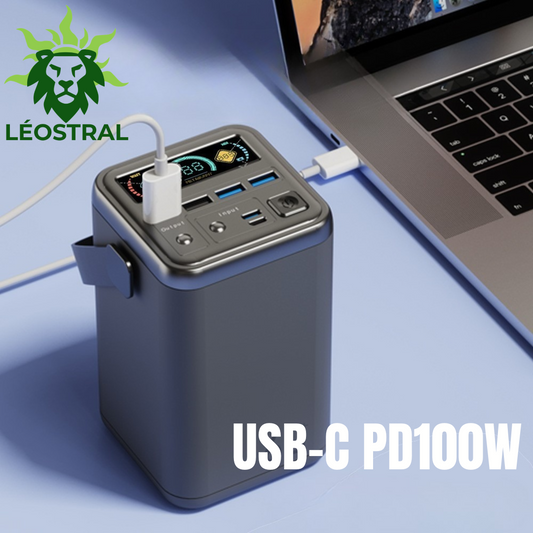 Image publicitaire de la batterie externe haute capacité LÉOSTRAL 60000mAh PD100W, connectée via un câble USB-C à un ordinateur portable ouvert sur un bureau. Un écran d'affichage numérique actif, des ports multiples et le texte "USB-C PD100W" en bas.